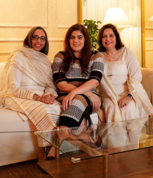 Three women in white sitting on a couch, engaged in conversation and displaying a sense of camaraderie.